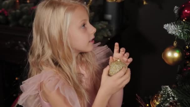Ein zehnjähriges Mädchen in der Nähe des Neujahrsbaums hält ein Neujahrsspielzeug in den Händen. Neues Jahr 2020. — Stockvideo