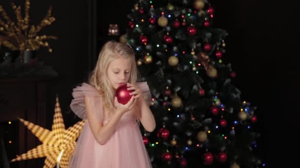 Una bambina di dieci anni vicino all'albero di Capodanno tiene in mano un giocattolo di Capodanno. Capodanno 2020 . — Video Stock