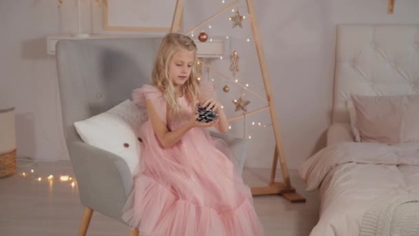 Ein neunjähriges Mädchen im Neujahrsdekor hält ein Neujahrsspielzeug in den Händen. Neues Jahr 2020. — Stockvideo