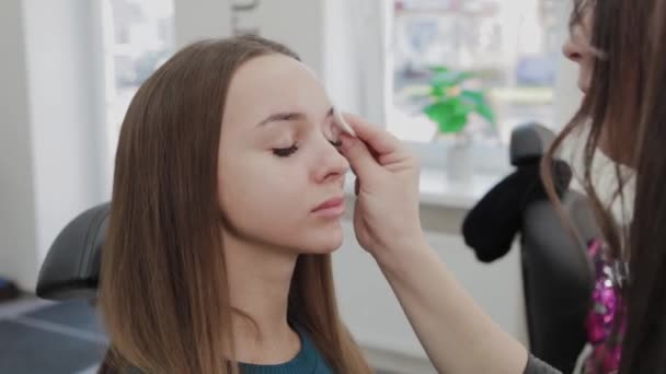 Artista de maquillaje profesional limpia a un cliente con una almohadilla de algodón sumergida en un gel especial . — Vídeo de stock