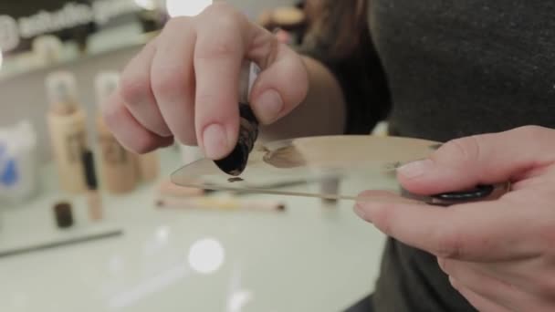 Maquilleuse professionnelle remuant la crème de maquillage sur une palette . — Video