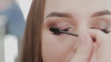Profesyonel makyöz kadın güzellik salonunun müşterisine kirpiklerini boyuyor..