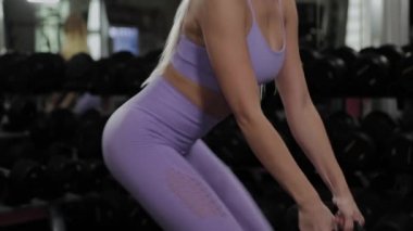 Güzel bir figürle atletik bir kadın spor salonunda bacak ve kalça simülatörü çalıştırıyor..