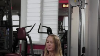 Güzel bir figürle atletik bir kadın spor salonunda bacak ve kalça simülatörü çalıştırıyor..