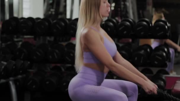 Αθλητική γυναίκα με όμορφη φιγούρα εκπαιδεύει τα πόδια και τους γλουτούς σε προσομοιωτή μπλοκ σε ένα γυμναστήριο. — Αρχείο Βίντεο