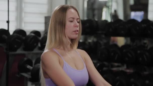 Αθλητική γυναίκα με όμορφη φιγούρα εκπαιδεύει τα πόδια και τους γλουτούς σε προσομοιωτή μπλοκ σε ένα γυμναστήριο. — Αρχείο Βίντεο