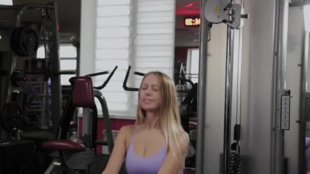 Mujer atlética con una hermosa figura entrena piernas y nalgas en un simulador de bloque en un gimnasio . — Vídeos de Stock