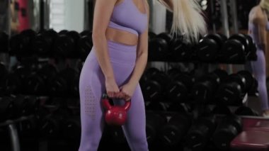 Güzel vücutlu atletik bir kadın spor salonunda bir su ısıtıcısıyla antrenman yapıyor..