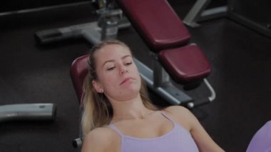 Güzel figürlü atletik bir kadın spor salonundaki simülatörde bacaklarını çalıştırıyor..