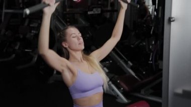 Güzel vücutlu atletik bir kadın spor salonundaki simülatörde sırtını eğitiyor..