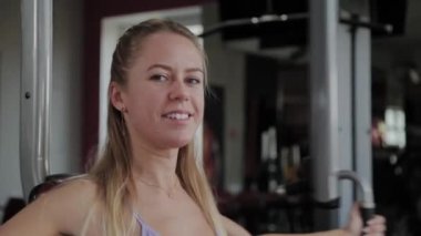 Güzel figürlü atletik bir kadın spor salonundaki simülatörde göğüs kaslarını çalıştırıyor..