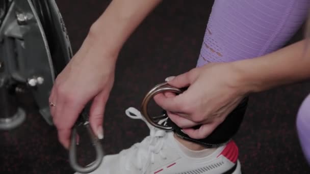 Atletische vrouw met een mooie figuur houdt haar been vast aan een blok fitnessapparaat in de sportschool. — Stockvideo
