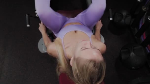 Athletic woman with a beautiful figure trains legs on the simulator in the gym. — Stock Video