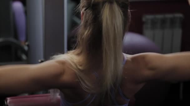 Αθλητική γυναίκα με μια όμορφη φιγούρα εκπαιδεύει την πλάτη της στον προσομοιωτή στο γυμναστήριο. — Αρχείο Βίντεο