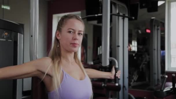 Donna atletica con una bella figura allena i muscoli pettorali sul simulatore in palestra . — Video Stock