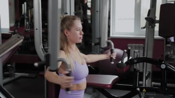 Femme sportive avec une belle silhouette entraîne les muscles pectoraux sur le simulateur dans la salle de gym . — Video