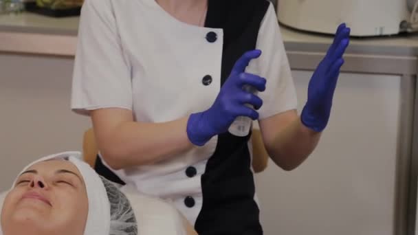 Estetista professionista tratta guanti di gomma blu con un antisettico. — Video Stock