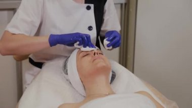 Profesyonel güzellik uzmanı ıslak mendille kadının yüzünü siler..