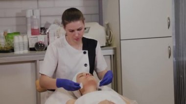 Profesyonel güzellik uzmanı ıslak mendille kadının yüzünü siler..