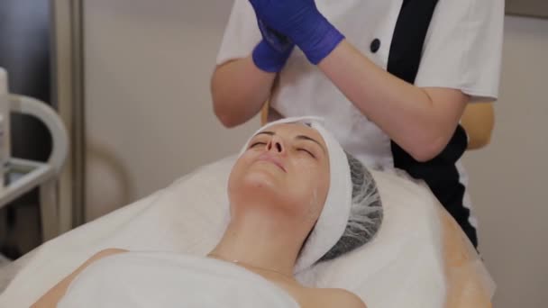 Professionele schoonheidsspecialiste brengt scrub olie op een vrouw gezicht met massage bewegingen van haar handen. — Stockvideo