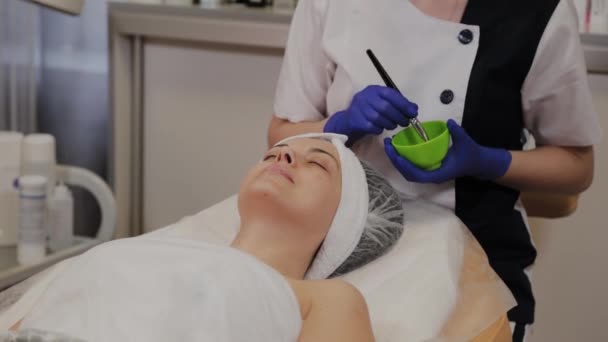 Profesional aplica una máscara facial a una mujer con un cepillo . — Vídeos de Stock