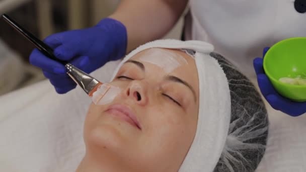 Professional applicerar en ansiktsmask på en kvinna med en borste. — Stockvideo