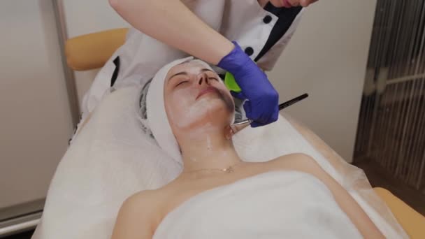 Professional applicerar en ansiktsmask på en kvinna med en borste. — Stockvideo