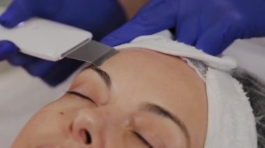 Profesyonel güzellik uzmanı orta yaşlı bir kadın için ultrasonik yüz temizliği yapıyor..