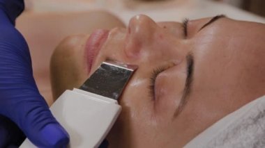 Profesyonel güzellik uzmanı orta yaşlı bir kadın için ultrasonik yüz temizliği yapıyor..