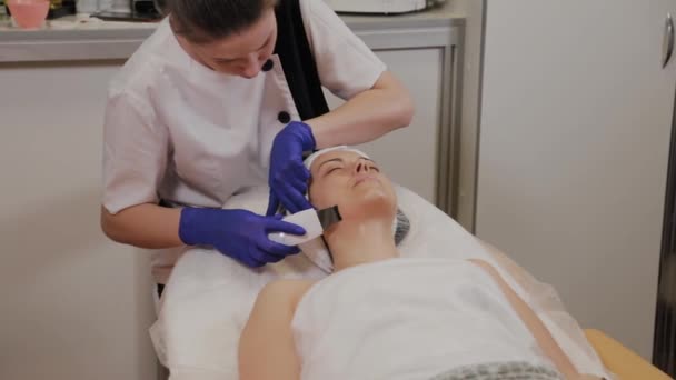 Професійний косметолог робить ультразвукове очищення обличчя для жінки середнього віку . — стокове відео