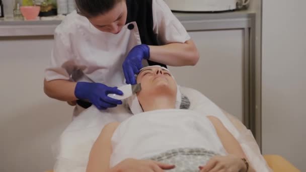Profesyonel güzellik uzmanı orta yaşlı bir kadın için ultrasonik yüz temizliği yapıyor.. — Stok video