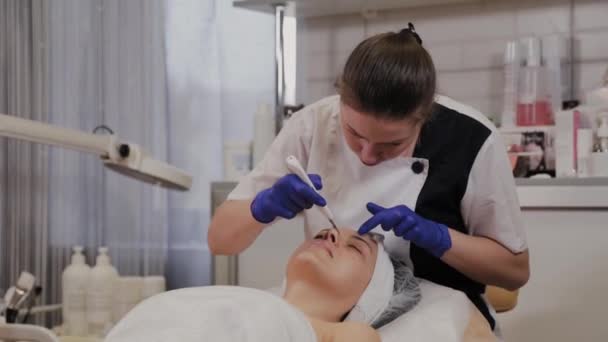 Professionele schoonheidsspecialiste doet ultrasone gezichtsreiniging voor vrouwen van middelbare leeftijd. — Stockvideo