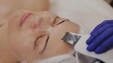 Profesyonel güzellik uzmanı orta yaşlı bir kadın için ultrasonik yüz temizliği yapıyor..