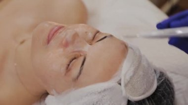Profesyonel güzellik uzmanı orta yaşlı bir kadın için ultrasonik yüz temizliği yapıyor..