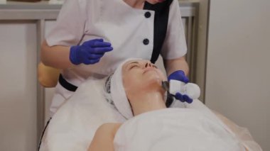 Profesyonel güzellik uzmanı orta yaşlı bir kadın için ultrasonik yüz temizliği yapıyor..