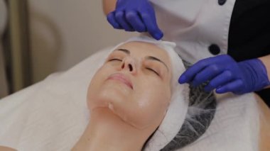 Profesyonel bir güzellik uzmanı kadın yüzünden şeffaf bir yaşlanma önleyici maske çıkarır..