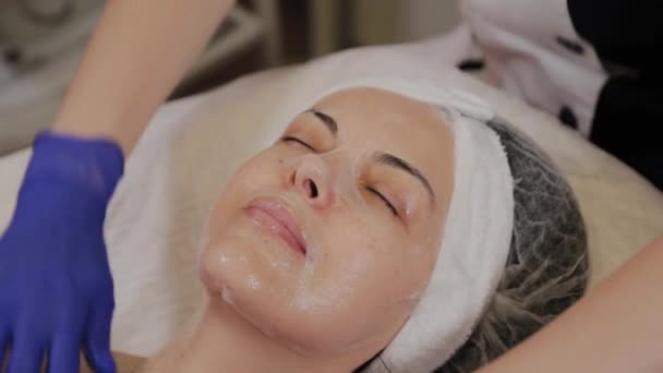 一位专业的美容师在脸上涂上透明的织物面罩. — 图库视频影像