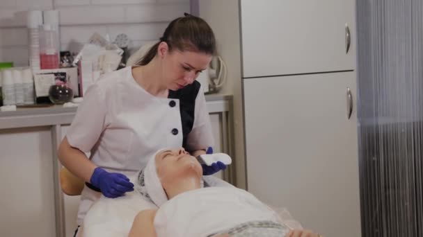 Професійний косметолог робить ультразвукове очищення обличчя для жінки середнього віку . — стокове відео