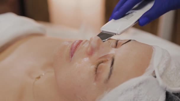 Professional beautician does ultrasonic face cleaning for middle-aged woman. — Stock Video