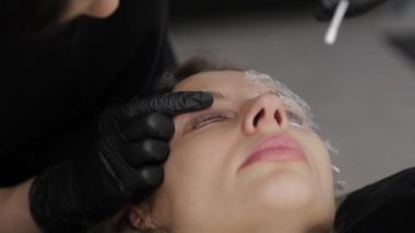 Güzellik salonunda çalışan profesyonel bir kozmetikçi kirpik jelini müşterinin kirpiklerine sürer..