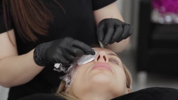 En professionell kosmetolog i en skönhetssalong tar bort en speciell film från ögonen på en kund. — Stockvideo
