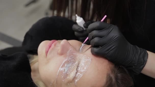 Um esteticista profissional em um salão de beleza aplicou um gel especial para laminação de pestanas em pestanas. . — Vídeo de Stock