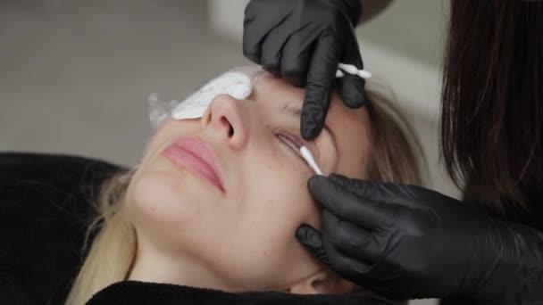 Um cosmetologista profissional em um salão de beleza aplica gel de laminação de pestanas às pestanas do cliente . — Vídeo de Stock