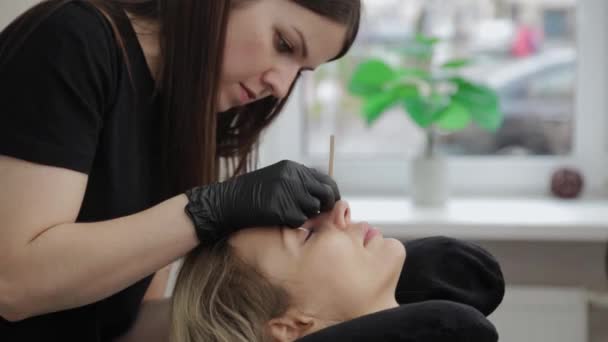 Професійний косметолог в салоні краси вирівнює вії клієнту . — стокове відео