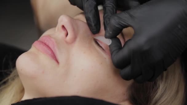 Esthéticienne professionnelle dans un salon de beauté colle une doublure en silicone pour la plastification des cils . — Video