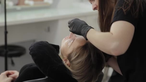 Professionele schoonheidsspecialiste in een schoonheidssalon schildert wimpers aan een klant. — Stockvideo