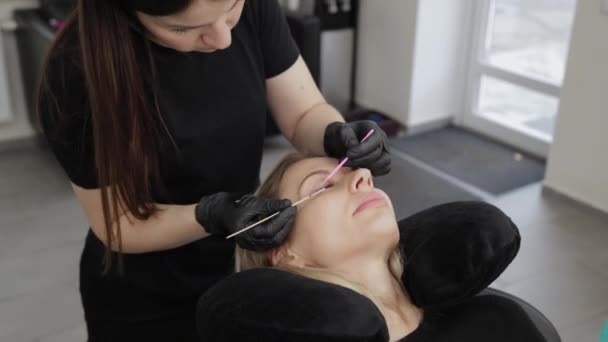 Professional beautician in a beauty salon straightens eyelashes to a client. — ストック動画