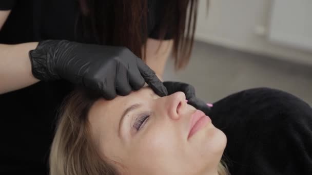 Professional beautician in a beauty salon straightens eyelashes to a client. — Stock Video