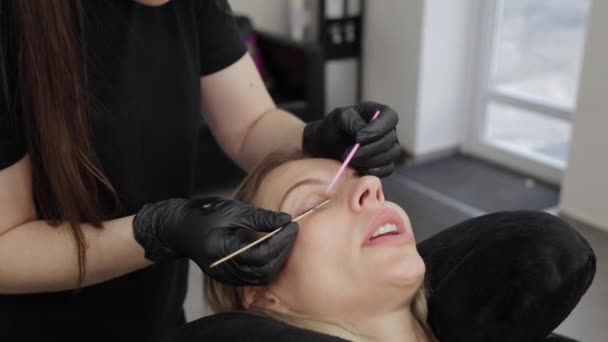 Professional beautician in a beauty salon straightens eyelashes to a client. — ストック動画