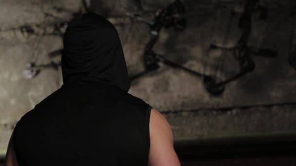 En man i svarta kläder tittar på väggen med rosetter och armborst. — Stockvideo